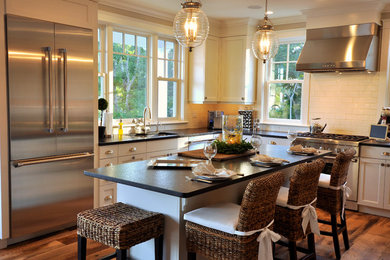 Open concept kitchen - mid-sized coastal u-shaped medium tone wood floor open concept kitchen idea in Boston with an undermount sink, granite countertops, white backsplash, ceramic backsplash, stainless steel appliances, white cabinets, an island and shaker cabinets