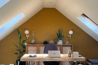 This is an example of a medium sized eclectic home office in Sussex with yellow walls, a freestanding desk, black floors and a feature wall.
