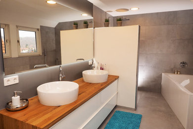 Kleines Modernes Duschbad mit flächenbündigen Schrankfronten, weißen Schränken, freistehender Badewanne, offener Dusche, grauen Fliesen, Zementfliesen, Zementfliesen für Boden, Aufsatzwaschbecken, Waschtisch aus Holz, grauem Boden und offener Dusche in Stuttgart