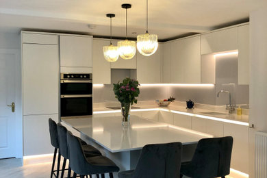 グラスゴーにある高級な広いコンテンポラリースタイルのおしゃれなキッチン (一体型シンク、フラットパネル扉のキャビネット、白いキャビネット、珪岩カウンター、グレーのキッチンパネル、ガラス板のキッチンパネル、黒い調理設備、クッションフロア、グレーの床、白いキッチンカウンター) の写真