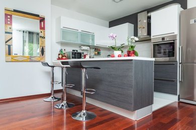 Mid-sized contemporary u-shaped eat-in kitchen in New York with an undermount sink, flat-panel cabinets, white cabinets, grey splashback, subway tile splashback, stainless steel appliances, painted wood floors and a peninsula.