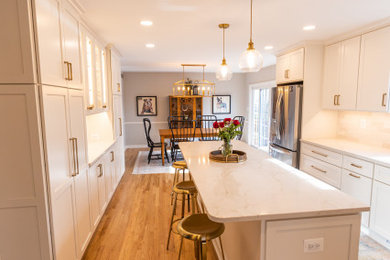 Example of a mid-sized classic l-shaped medium tone wood floor and brown floor eat-in kitchen design in Baltimore with an undermount sink, shaker cabinets, white cabinets, quartz countertops, white backsplash, porcelain backsplash, stainless steel appliances, an island and white countertops