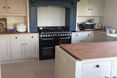 Inspiration for a mid-sized traditional u-shaped open plan kitchen in Wiltshire with shaker cabinets, beige cabinets, wood benchtops, white splashback and with island.