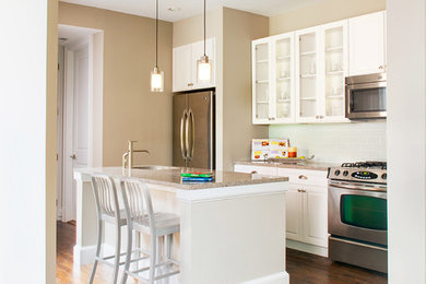 Mid-sized contemporary single-wall eat-in kitchen in DC Metro with a drop-in sink, glass-front cabinets, white cabinets, laminate benchtops, green splashback, glass tile splashback, stainless steel appliances, dark hardwood floors, with island, brown floor and beige benchtop.