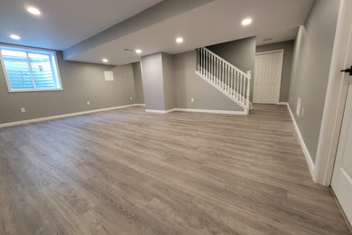 Large trendy walk-out laminate floor, brown floor and coffered ceiling basement photo in Detroit with beige walls and a home theater
