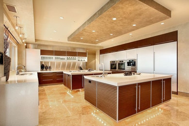 This is an example of a large contemporary u-shaped eat-in kitchen in Los Angeles with a double-bowl sink, red cabinets, quartz benchtops, multi-coloured splashback, stone slab splashback, stainless steel appliances, travertine floors and multiple islands.
