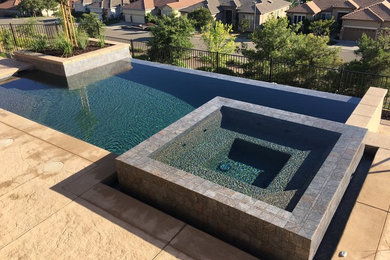 Photo of a mid-sized contemporary backyard rectangular infinity pool in Sacramento with a hot tub and stamped concrete.