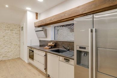 Photo of a mid-sized modern single-wall eat-in kitchen in Other with a single-bowl sink, white cabinets, multi-coloured splashback, stainless steel appliances, light hardwood floors, no island, brown floor and grey benchtop.