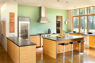 Large trendy u-shaped concrete floor eat-in kitchen photo in Other with flat-panel cabinets, medium tone wood cabinets, green backsplash, an island, an undermount sink, glass tile backsplash and stainless steel appliances