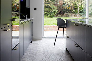 Design ideas for a large contemporary open plan kitchen in Kent with a built-in sink, flat-panel cabinets, blue cabinets, composite countertops, metallic splashback, glass tiled splashback, black appliances, porcelain flooring, an island, grey floors and white worktops.