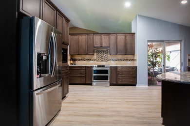 Inspiration for a mid-sized transitional kitchen remodel in Jacksonville with a farmhouse sink, recessed-panel cabinets, dark wood cabinets, granite countertops, stone tile backsplash, stainless steel appliances and multicolored countertops