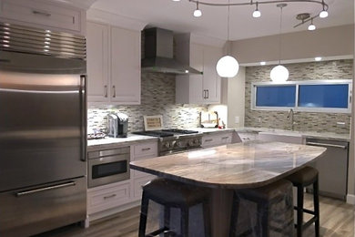 This is an example of a small transitional l-shaped open plan kitchen in Hawaii with a farmhouse sink, beaded inset cabinets, white cabinets, granite benchtops, grey splashback, glass tile splashback, stainless steel appliances, porcelain floors, with island and grey floor.