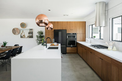 Example of a large trendy l-shaped concrete floor and gray floor kitchen design in Phoenix with an undermount sink, flat-panel cabinets, medium tone wood cabinets, solid surface countertops, white backsplash, ceramic backsplash, black appliances, an island and white countertops
