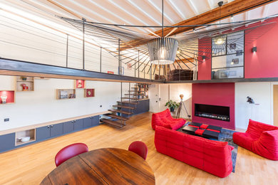 Diseño de salón abierto urbano grande con paredes rojas, suelo de madera clara, todas las chimeneas y vigas vistas