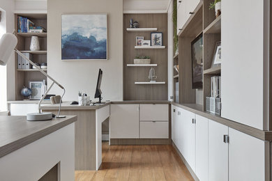 Medium sized contemporary study in Manchester with white walls, medium hardwood flooring, a built-in desk and brown floors.