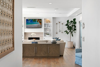 Family room - transitional open concept medium tone wood floor family room idea in Orange County with white walls, a standard fireplace and a wall-mounted tv