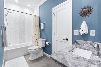 Ejemplo de cuarto de baño único clásico renovado con combinación de ducha y bañera, encimeras multicolor, armarios con rebordes decorativos, puertas de armario blancas, paredes azules, suelo de baldosas de porcelana, lavabo bajoencimera, encimera de granito, suelo gris y hornacina