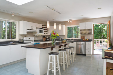 Inspiration for a large beach style l-shaped eat-in kitchen in Vancouver with a double-bowl sink, flat-panel cabinets, white cabinets, wood benchtops, white appliances, with island, grey splashback, matchstick tile splashback and ceramic floors.