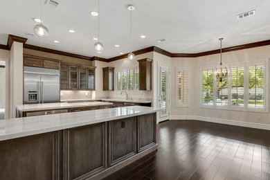 Example of a huge transitional dark wood floor and brown floor eat-in kitchen design in Las Vegas with an undermount sink, recessed-panel cabinets, brown cabinets, quartzite countertops, beige backsplash, mosaic tile backsplash, stainless steel appliances, two islands and gray countertops