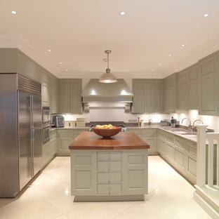 Imagen de cocina tradicional, grande, con fregadero bajoencimera, armarios con paneles con relieve, puertas de armario verdes, encimera de piedra caliza, salpicadero blanco, electrodomésticos de acero inoxidable, suelo de piedra caliza y una isla