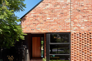 Mid-sized contemporary one-storey brick red house exterior in Geelong with a gable roof, a metal roof and a black roof.