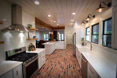 Kitchen - cottage l-shaped brick floor kitchen idea in New Orleans with a farmhouse sink, shaker cabinets, white cabinets, quartz countertops, white backsplash, subway tile backsplash, stainless steel appliances and an island