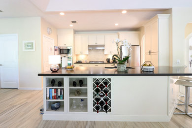 Photo of a mid-sized transitional u-shaped eat-in kitchen in Houston with an undermount sink, recessed-panel cabinets, white cabinets, soapstone benchtops, white splashback, subway tile splashback, stainless steel appliances, porcelain floors, with island, beige floor and black benchtop.