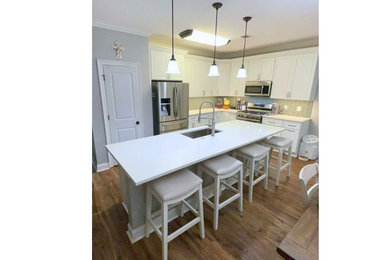 Trendy laminate floor and brown floor kitchen photo in New Orleans with a drop-in sink, raised-panel cabinets, white cabinets, quartzite countertops, green backsplash and white countertops