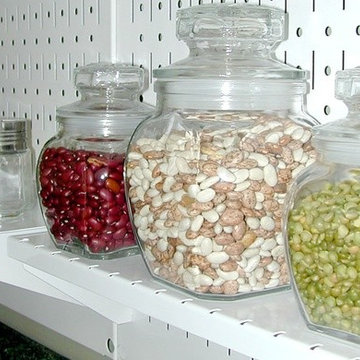 A Wall Control pegboard shelf being used to organize jars of food over a sink