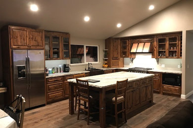 Mid-sized mountain style l-shaped medium tone wood floor and brown floor eat-in kitchen photo in Sacramento with a farmhouse sink, glass-front cabinets, distressed cabinets, granite countertops, stainless steel appliances, an island and white countertops