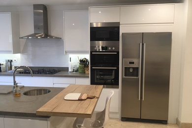 Example of a mid-sized trendy u-shaped kitchen design in Other with flat-panel cabinets, white cabinets, stainless steel appliances and an island