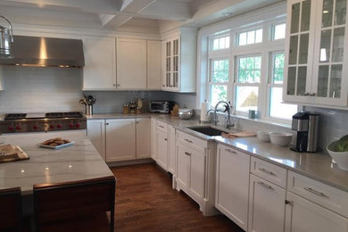 Enclosed kitchen - mid-sized transitional u-shaped medium tone wood floor and brown floor enclosed kitchen idea in New York with a single-bowl sink, shaker cabinets, white cabinets, white backsplash, glass tile backsplash, stainless steel appliances and an island