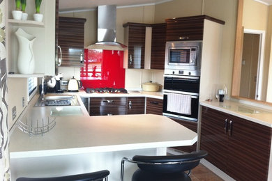 Inspiration for a small modern l-shaped kitchen/diner in Devon with a built-in sink, flat-panel cabinets, brown cabinets, quartz worktops, red splashback, glass sheet splashback, stainless steel appliances, ceramic flooring and a breakfast bar.