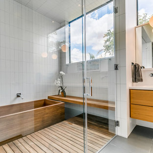 Ispirazione per una stanza da bagno padronale minimalista di medie dimensioni con ante lisce, ante in legno scuro, vasca giapponese, vasca/doccia, piastrelle bianche, piastrelle in ceramica, pareti bianche, pavimento con piastrelle in ceramica, lavabo sottopiano, top in quarzo composito, pavimento grigio e porta doccia a battente