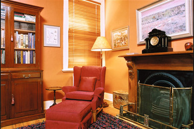 Imagen de despacho clásico pequeño con biblioteca, paredes rojas, suelo de madera clara, todas las chimeneas, marco de chimenea de madera, escritorio independiente y suelo marrón