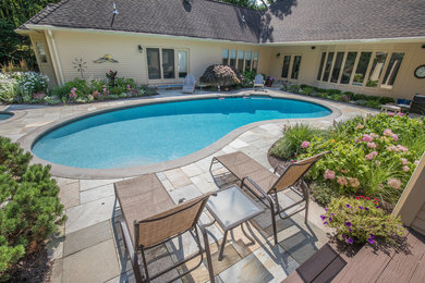 Photo of a large traditional backyard kidney-shaped lap pool in New York with a hot tub and tile.