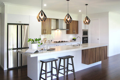 This is an example of a large contemporary single-wall kitchen in Brisbane with an undermount sink, medium wood cabinets, white splashback, glass tile splashback, panelled appliances, dark hardwood floors and with island.