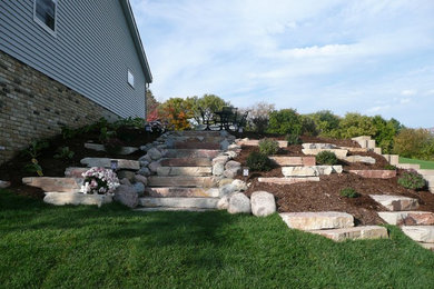 Expansive country sloped full sun formal garden in Milwaukee with a retaining wall and natural stone pavers.