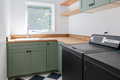 Example of a mid-sized transitional l-shaped marble floor and multicolored floor dedicated laundry room design in Portland with shaker cabinets, green cabinets, wood countertops, white walls, a side-by-side washer/dryer and brown countertops