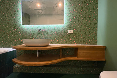 Immagine di una piccola stanza da bagno minimal con nessun'anta, ante in legno chiaro, vasca da incasso, WC a due pezzi, pareti verdi, pavimento in cemento, lavabo a bacinella, top in legno, pavimento verde, un lavabo, mobile bagno sospeso e carta da parati