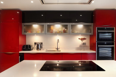 This is an example of a medium sized modern open plan kitchen in Buckinghamshire with a submerged sink, flat-panel cabinets, red cabinets, quartz worktops, white splashback, black appliances, an island, white worktops, laminate floors, beige floors and feature lighting.