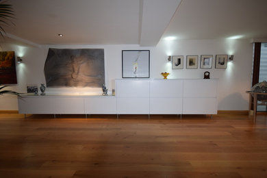 Diseño de salón abierto actual grande sin chimenea y televisor con paredes blancas, suelo de madera en tonos medios y suelo marrón