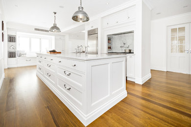 Traditional kitchen in Sydney with a farmhouse sink, white cabinets, marble benchtops, stainless steel appliances, medium hardwood floors and with island.