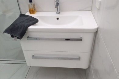 Design ideas for a small modern 3/4 bathroom in Melbourne with white cabinets, a corner shower, white tile, porcelain tile, white walls, porcelain floors, an integrated sink, solid surface benchtops, white floor, a hinged shower door and white benchtops.