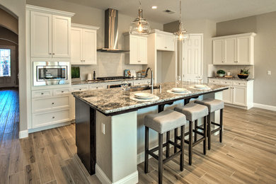 Example of a cottage l-shaped porcelain tile and gray floor kitchen design in Other with an undermount sink, recessed-panel cabinets, white cabinets, granite countertops, white backsplash, limestone backsplash, stainless steel appliances and an island