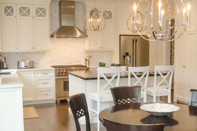 Example of a mid-sized classic medium tone wood floor and brown floor eat-in kitchen design in Toronto with an undermount sink, shaker cabinets, white cabinets, quartz countertops, white backsplash, stone tile backsplash, stainless steel appliances and an island