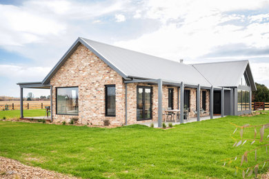 This is an example of a large country one-storey brick grey house exterior in Canberra - Queanbeyan with a gable roof, a metal roof and a grey roof.