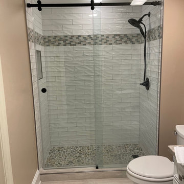 3x12 textured subway tile, with a darker mosaic band and pebble shower floor.