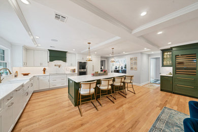 L-shaped light wood floor and coffered ceiling open concept kitchen photo in New York with a farmhouse sink, shaker cabinets, white cabinets, quartz countertops, white backsplash, quartz backsplash, stainless steel appliances, an island and white countertops