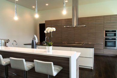 Design ideas for a large modern galley open plan kitchen in Philadelphia with an undermount sink, flat-panel cabinets, grey cabinets, solid surface benchtops, white splashback, stainless steel appliances, dark hardwood floors, multiple islands, brown floor and white benchtop.
